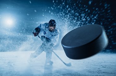 An ice hockey player hitting a hockey puck on an ice hockey field.