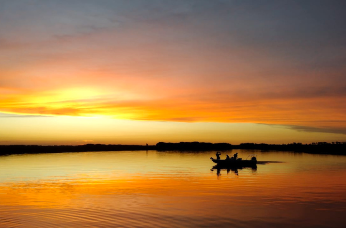 Silhouetted boat on tranquil water under a vibrant sunset sky in the Parana Delta.