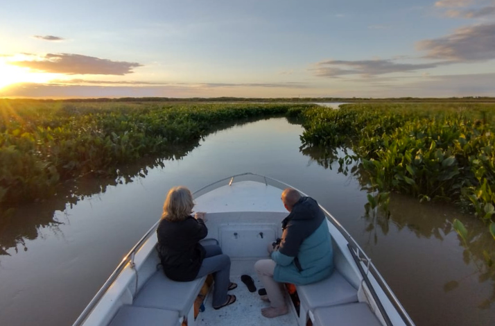 A couple in a boat glide through lush waterways at sunset in the Parana Delta Biosphere Reserve.