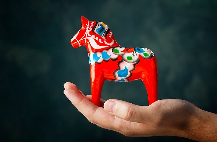 Promotional photo of a hand holding a vibrant red authentic Dala horse.