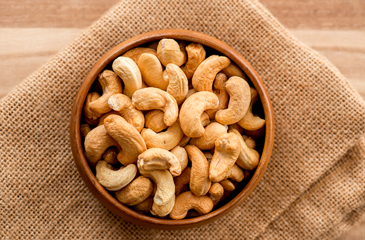 Bowl of roasted cashew nuts on a burlap cloth.