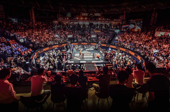 The interior of Rajadamnern Stadium filled with spectators on a Thai boxing match, as viewed from the VIP lounge.