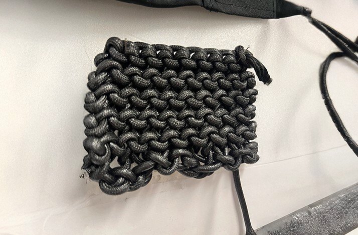 Close-up of a chunky dark woven latex bracelet resting on a white surface, handcrafted by HADERLUMP.