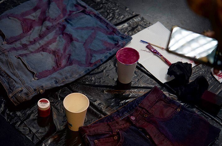 Denim fabric, magenta dye, brushes, and craft supplies spread on a black plastic sheet during a hands-on design workshop.