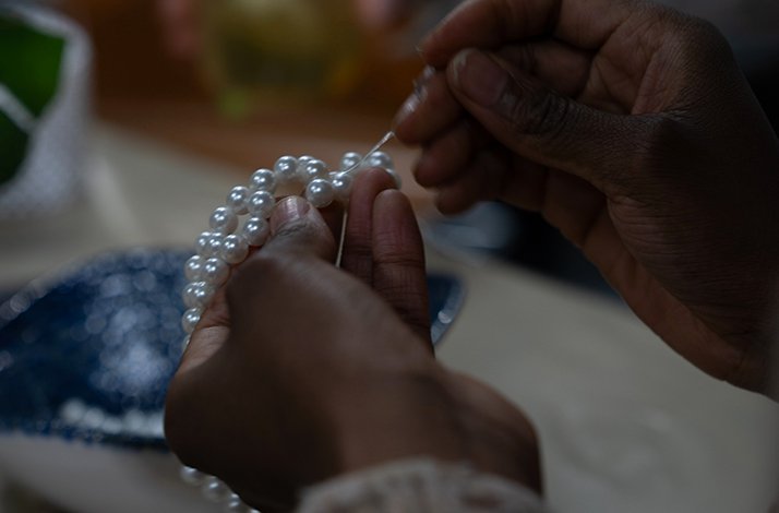 Hands carefully threading white pearls onto a string, assembling a multi-strand pearl necklace.