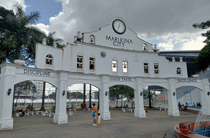 Marikina City landmark arch with clock, people, and benches in a public park.