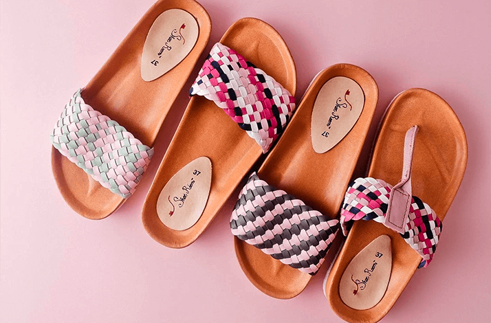 Four of colorful, woven sandals on a pink background.