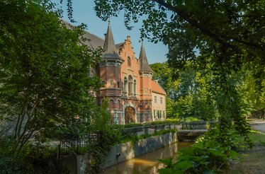 The beautiful entrance to Kasteel Steenenburg surrounded by greenery, as viewed from a near road approaching the entrance.
