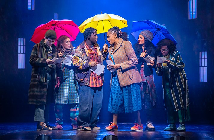 Cast members sing together under colourful umbrellas in a lively Paddington musical scene
