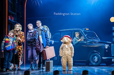 Paddington Bear arrives at Paddington Station in a lively West End musical scene.