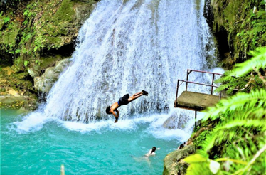 Adventurer diving into a waterfall pool, capturing the thrill of the Hill & Gully rivers and caves tour.