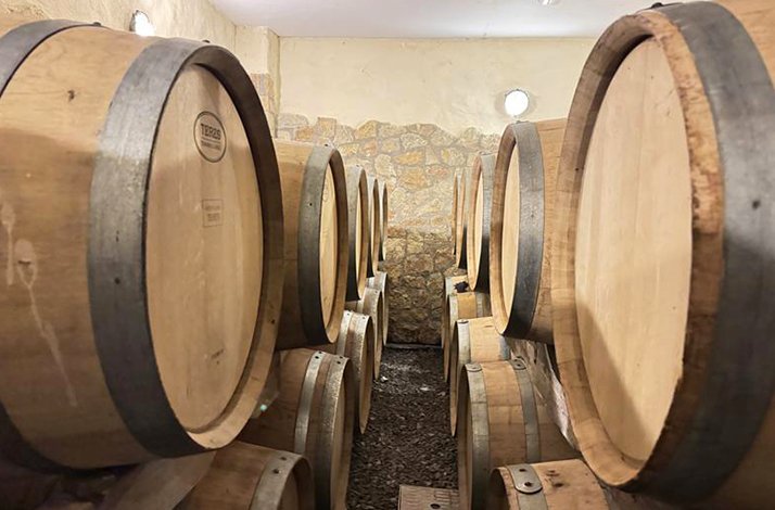 Rows of wooden wine barrels stacked in a stone-walled cellar.