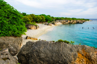 Kokomo Beach in Curaçao with rocky shoreline, clear water, and green trees.