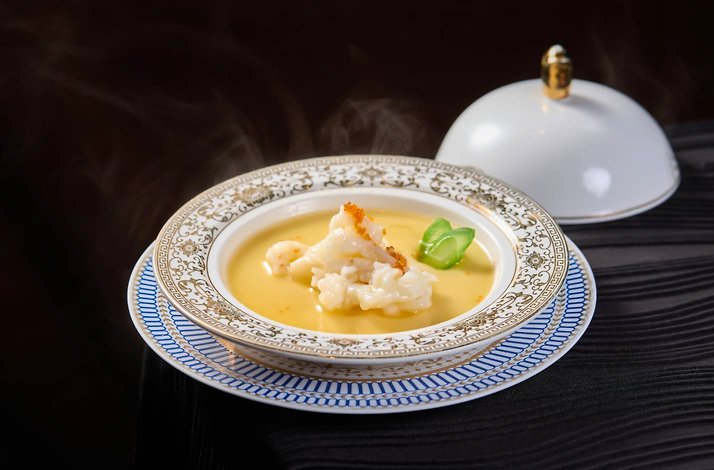 A gourmet lobster dish topped with roe served in an ornate blue and gold rimmed bowl.