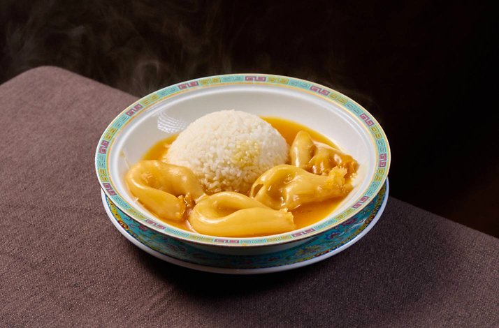A steaming bowl of bird's nest congee with partridge and white rice in a rich golden broth.