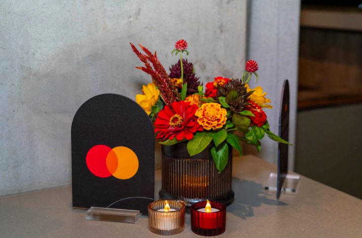 Stand with Mastercard logo next to flowers and candles in Mastercard colors on a table at the Moody Center.