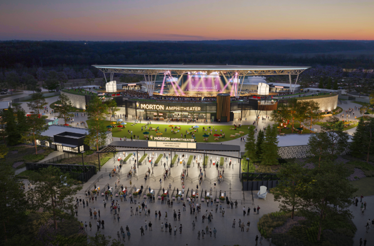 Crowds enter Morton Amphitheater at sunset for a live outdoor concert, with stage lights illuminating the venue.