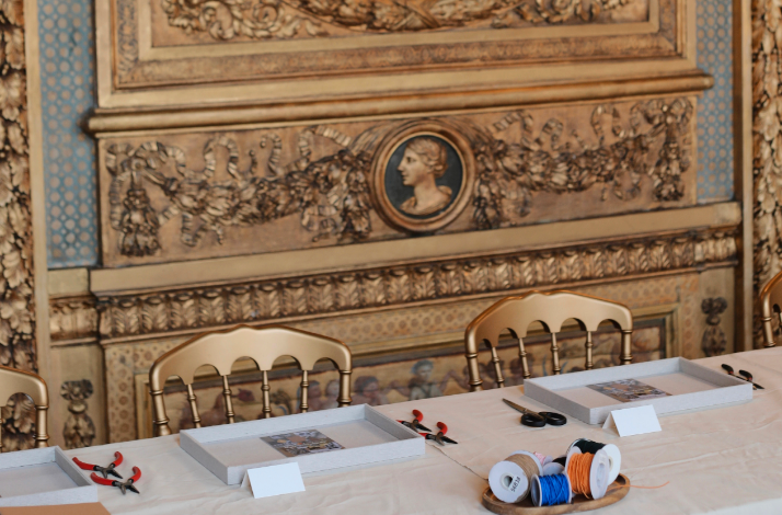 Craft workshop setup at Hôtel de Lauzun with tools, trays, and spools of thread on a long table.