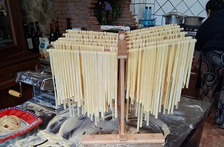Fresh pasta strips hanging on a wooden drying rack in a kitchen.