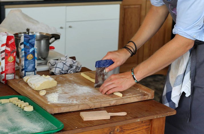 A person is skillfully cutting dough on a wooden cutting board in a well-lit kitchen.