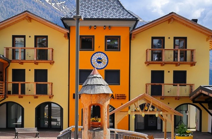 Yellow-orange alpine building with balconies and a clock.