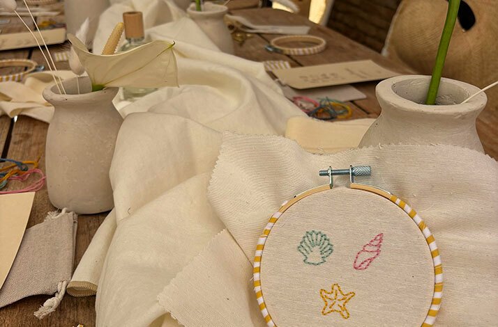 Embroidery hoop with stitched seashells and starfish on a workshop table with supplies.