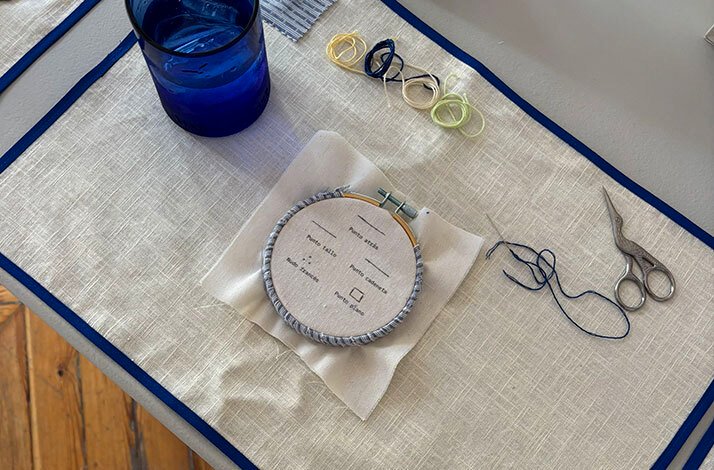 Embroidery hoop, threads, scissors, and a glass set up for stitching practice.
