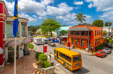Colorful town street with shops, cars, and a yellow bus in Holetown, Barbados.