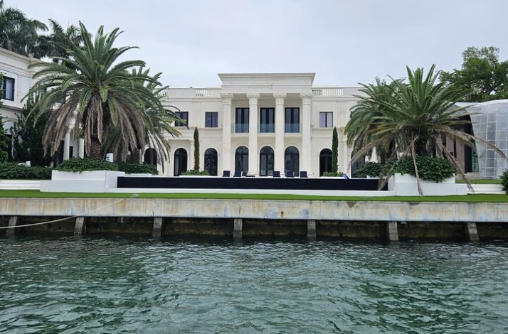 Large waterfront mansion with palm trees along the seawall.