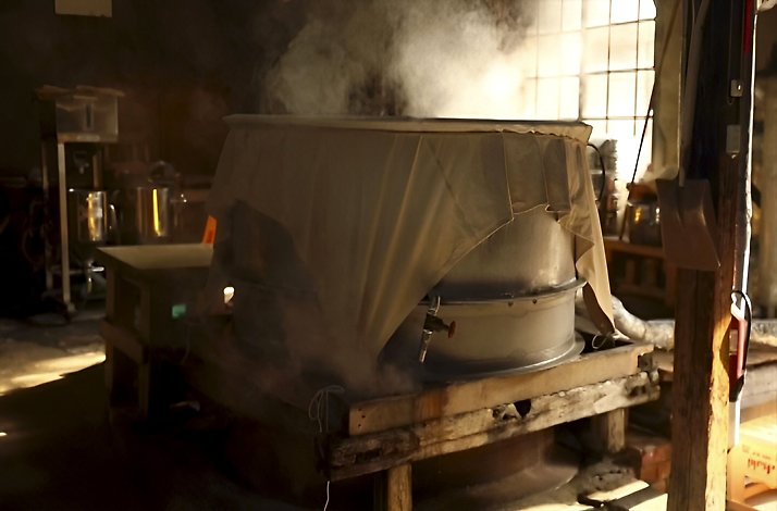 Traditional sake brewing process with steam rising from a covered vat at Fumigiku Shuzo brewery.