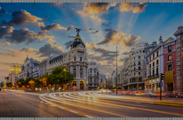 Madrid's Gran Vía at dusk with illuminated buildings, light trails, and a dramatic sunset sky.