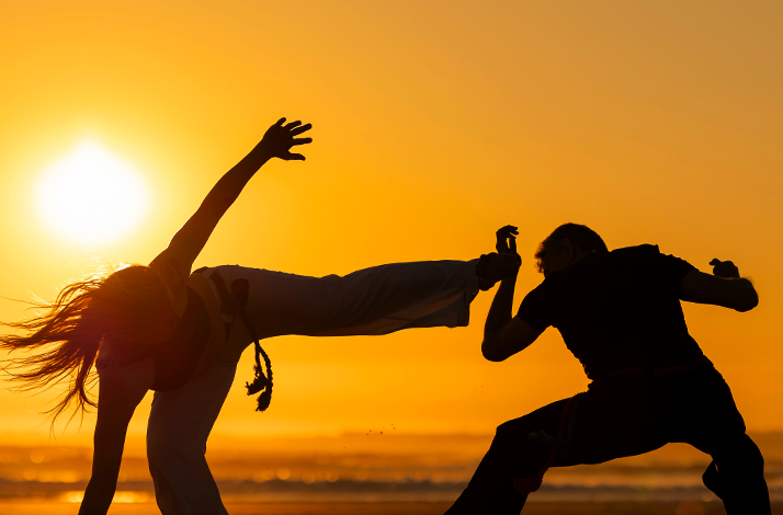 Capoeira practice on the beach at sunset with dynamic movements.