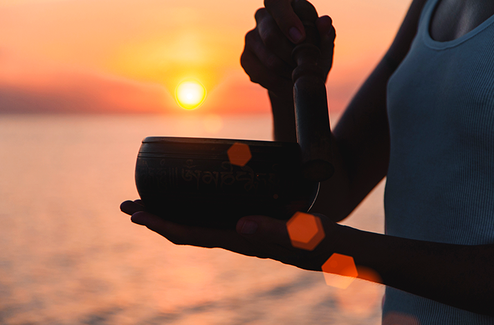 Hands holding a sound bowl at sunset by the ocean