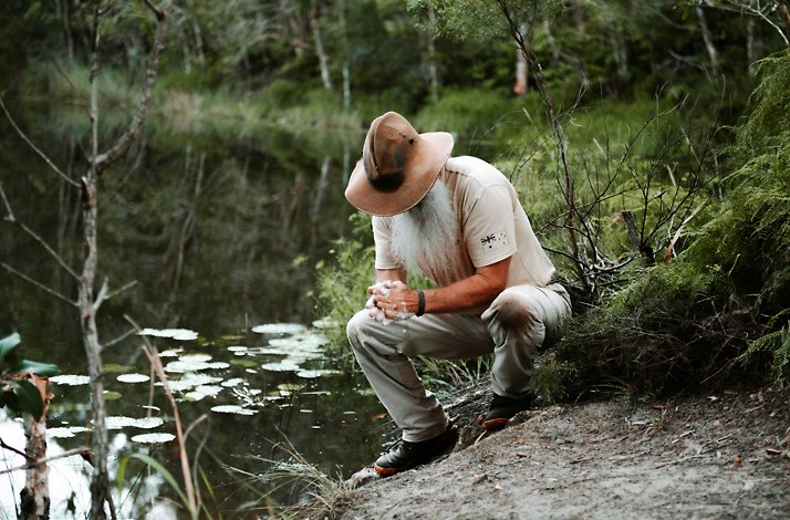 An outdoor survivalist Rick J. Petersen at the edge of a calm pond.