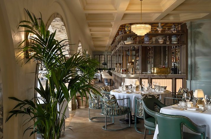 Elegant dining room at Ristorante Loren with green velvet chairs, palm plants, and a marble bar.