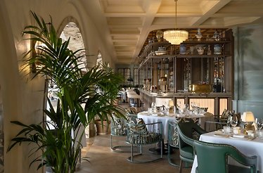 Elegant dining room at Ristorante Loren with green velvet chairs, palm plants, and a marble bar.