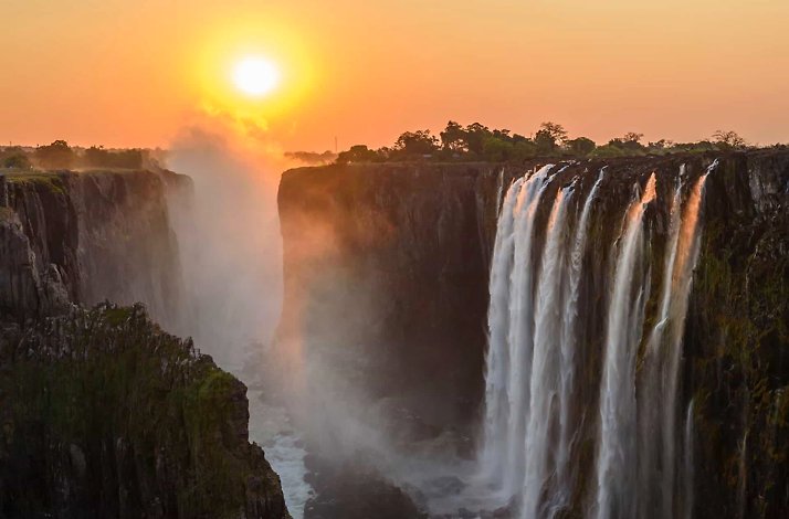 Victoria Falls cascading dramatically in Zambia, Africa, surrounded by lush greenery and mist rising from the water.