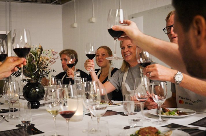 Guests raise their glasses around the table, celebrating their shared culinary experience with food, wine and good company.