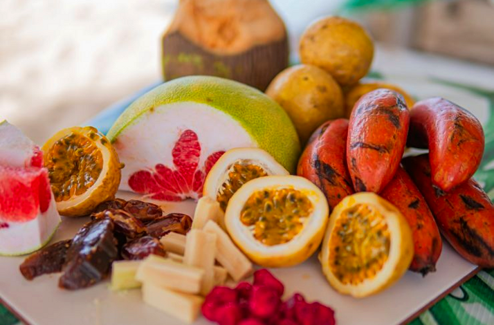 Plate of tropical fruits including watermelon, passion fruit, dates, pomelo, and Zanzibar red bananas.