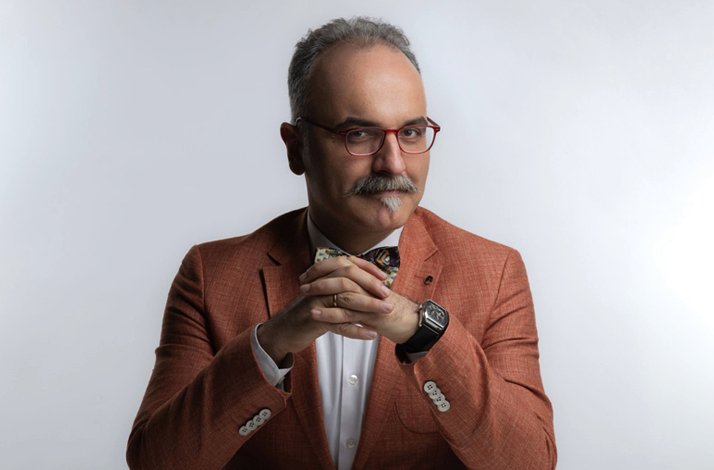 A close-up shot of historian Emrah Safa Gürkan posing with his hands clasped on the table.