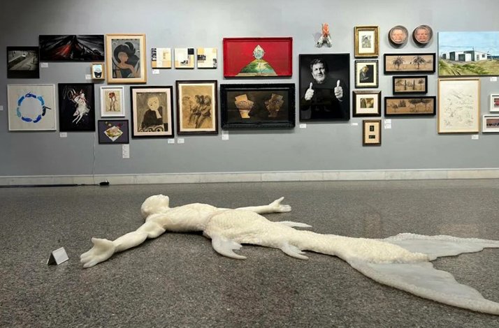 Image of many paintings from the Taviloğlu collection displayed on the wall and on the floor is an artwork that appears to depict a human and a mermaid together.