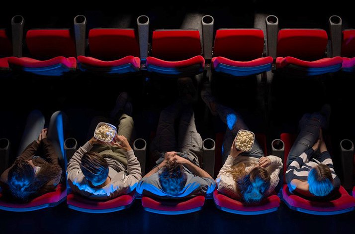 Top-down view of people sitting in red seats of ODEON cinema with bowls of popcorn.