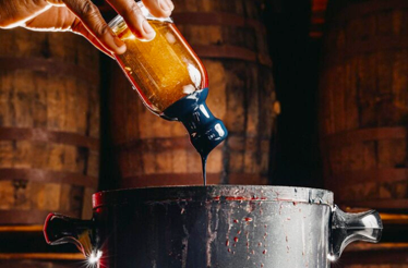 A person pouring a liquid into a pot containing whiskey, focusing on the interaction between the two elements.
