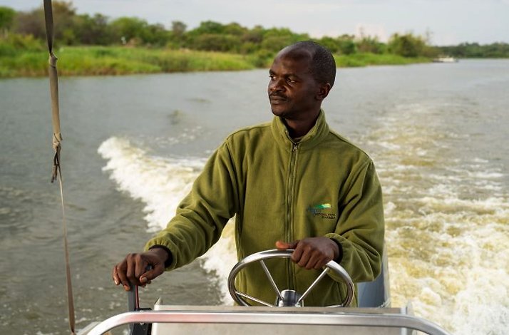 Person operating a boat on a calm river during a boat safari at a game lodge.