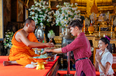  A monk in traditional orange robes is performing a spiritual ritual with visitors.