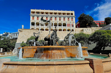Fountain with bronze figures in front of a multi‑story historic building.