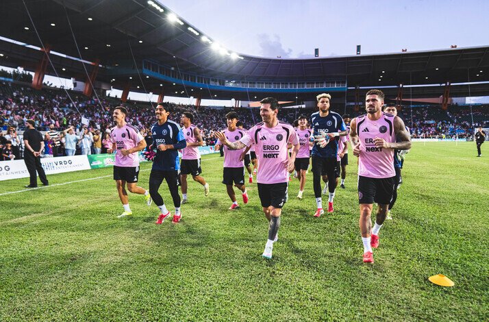 Inter Miami CF players jogging and warming up on the pitch before a game, with fans in the stadium.
