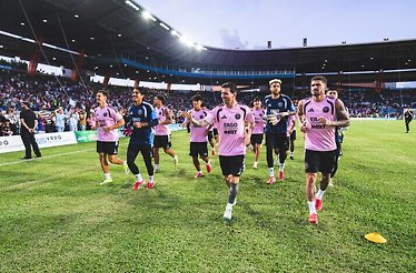 Inter Miami CF players jogging and warming up on the pitch before a game, with fans in the stadium.