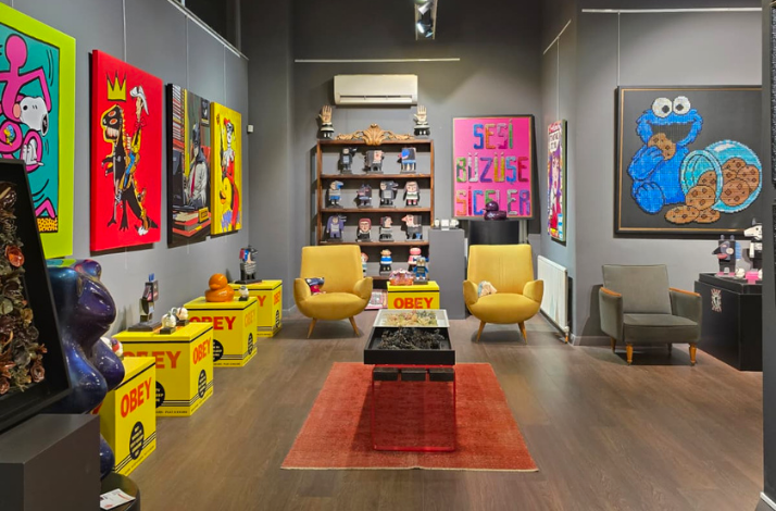 Interior of Red Art İstanbul decorated with pop-art paintings, collectible figures, mustard-yellow armchairs and a central table on a red rug