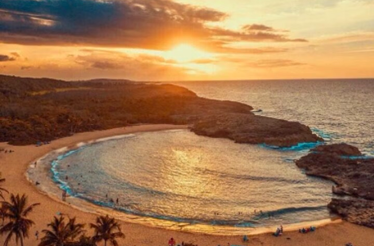 Golden sunset over Mar Chiquita Beach, with people swimming and relaxing in the crescent-shaped bay surrounded by rocky outcrops.